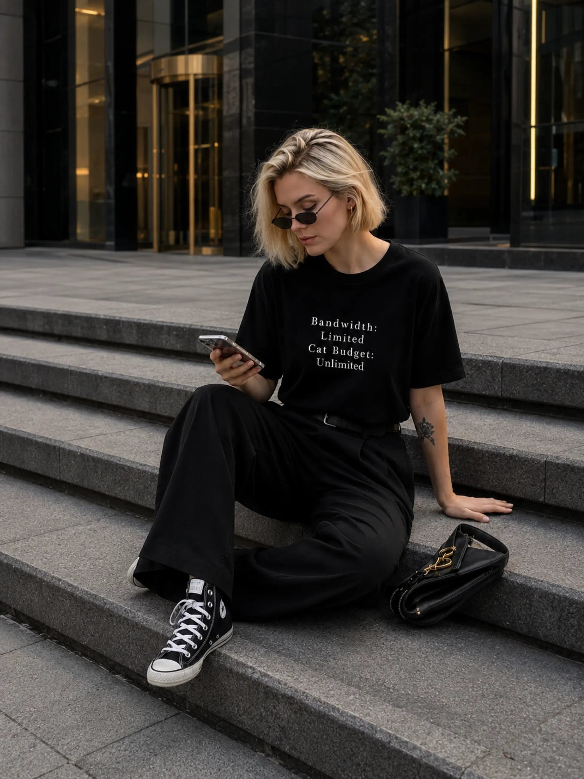 Woman sitting on steps wearing a black t-shirt with text, using a phone.